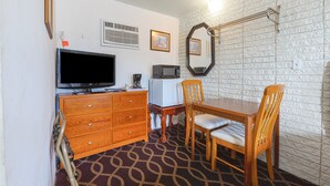 A room with a wooden dresser, a television, a microwave, a dining table with chairs, and a patterned carpet. - Sonrise Inn Lincoln Hwy By OYO (Breezewood)