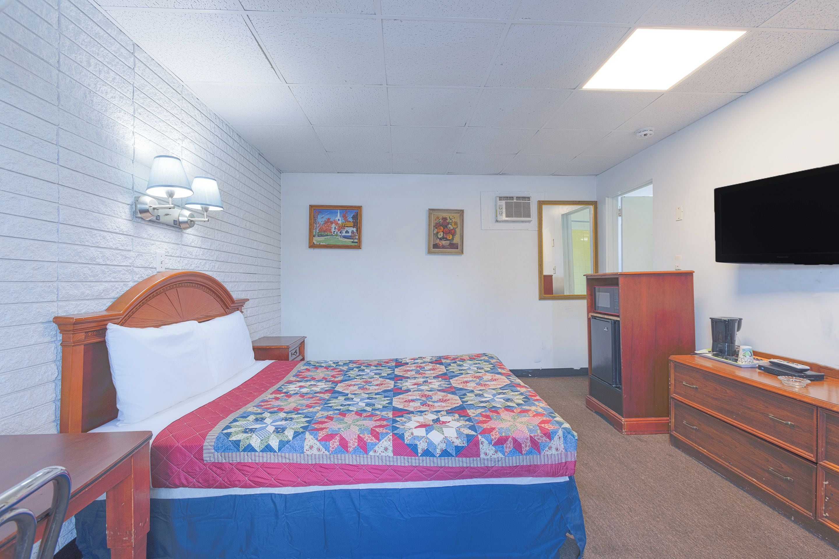 A hotel room with a bed, a dresser, a television, and a painting on the wall.