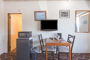Quarto de hotel com mesa de jantar de madeira, quatro cadeiras, televisão, micro-ondas e lixeira.