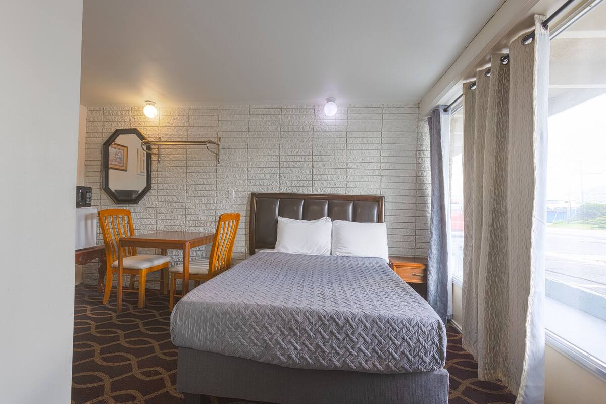 Una camera d'albergo con un letto, una scrivania e una sedia. Presente una finestra con tende e vista sull'esterno.