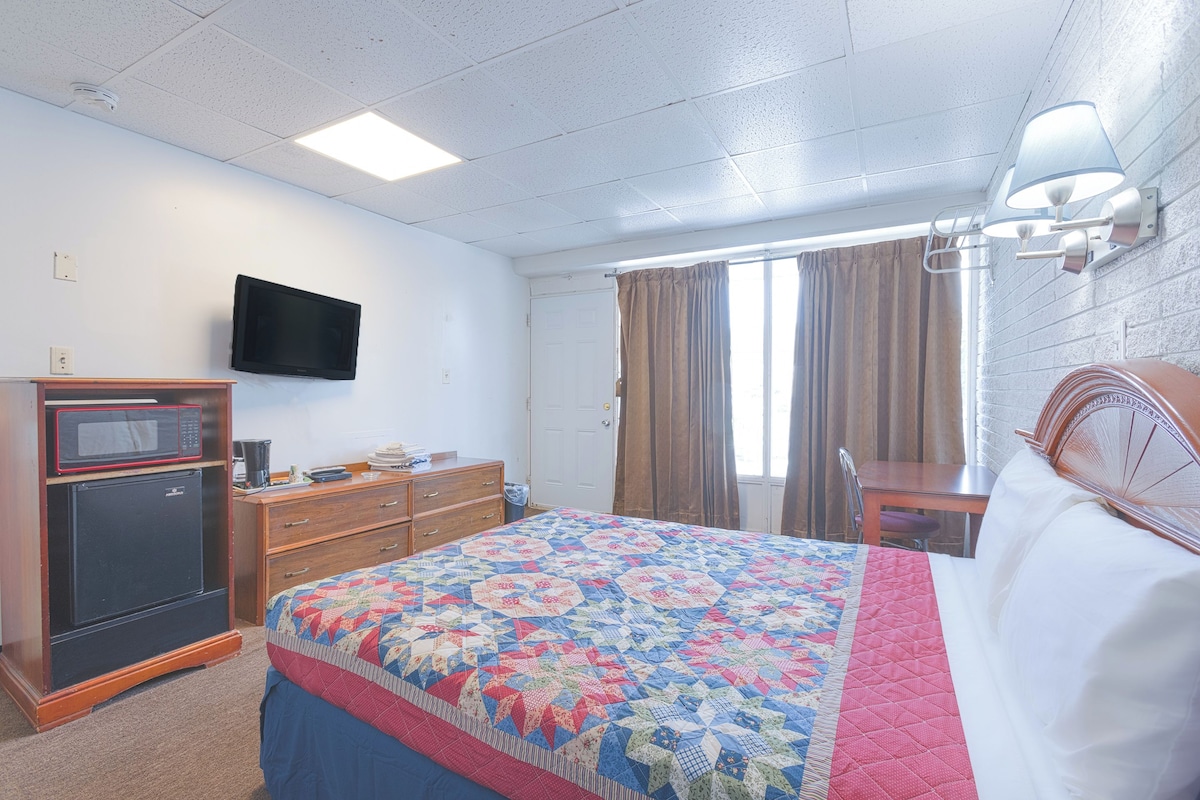 A hotel room with a bed, a television, a microwave, a dresser, and a window with curtains.