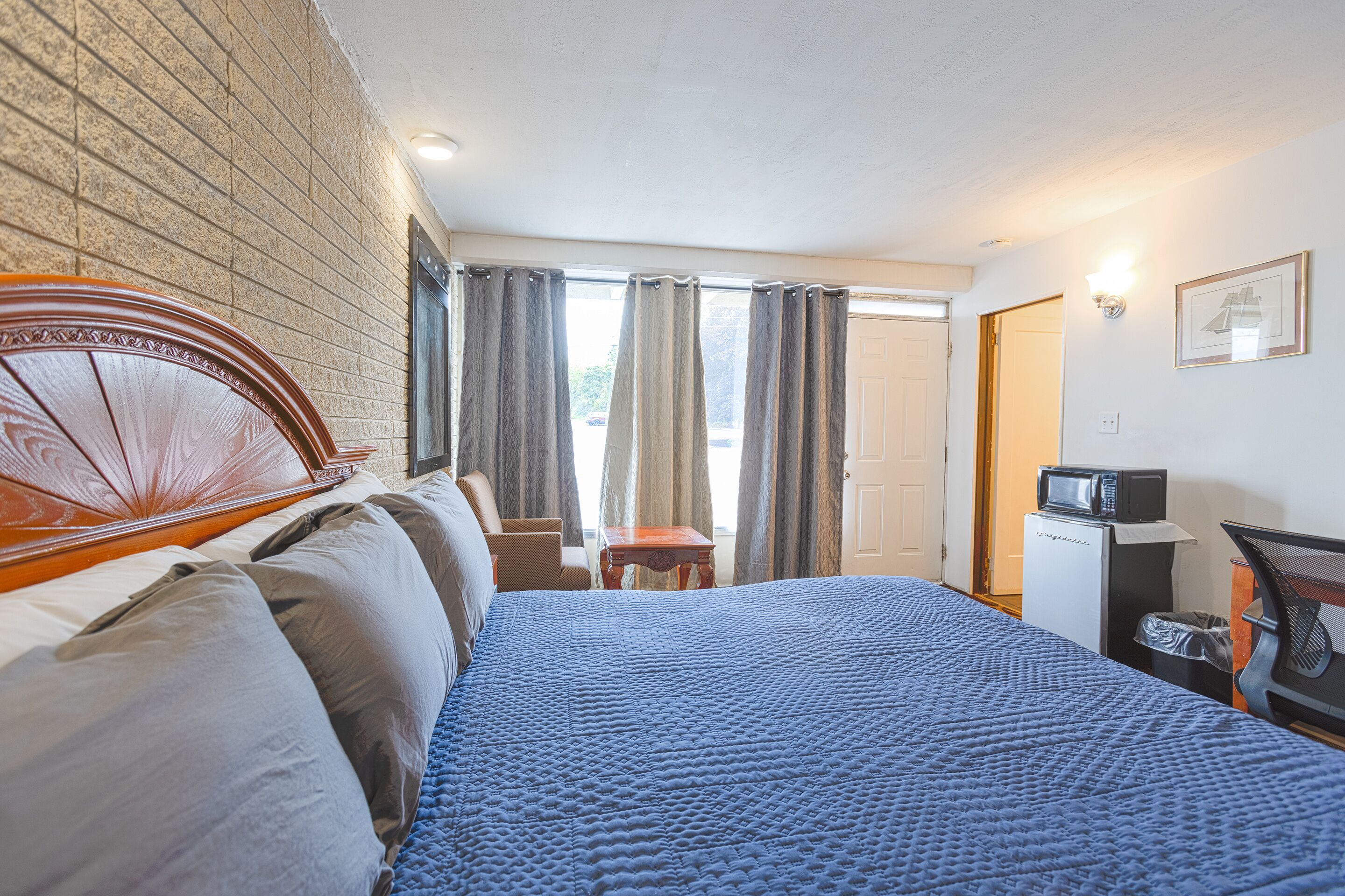 Habitación de hotel con una cama grande, un cabecero de madera, una mesita pequeña, un microondas y un cubo de basura.