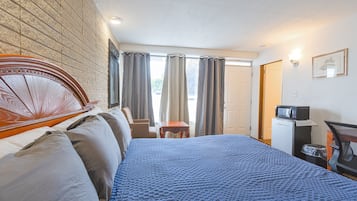 Habitación de hotel con una cama grande, un cabecero de madera, una mesita pequeña, un microondas y un cubo de basura.