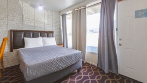 A hotel room with a bed, a headboard, a window with curtains, and a door. - Sonrise Inn Lincoln Hwy By OYO (Breezewood)
