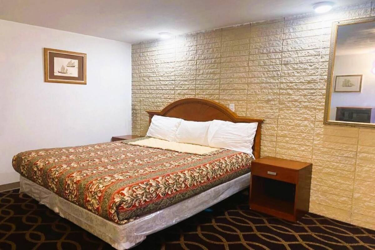 Una camera d'albergo con un letto, un comodino, uno specchio fissato alla parete e un quadro incorniciato.