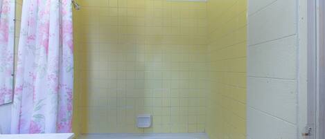 Une salle de bain avec des murs recouverts de carreaux jaunes, une baignoire blanche et un rideau de douche à motifs floraux.
