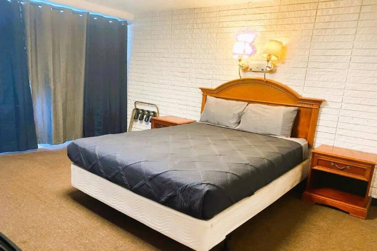 Un letto rifatto con un poggiatesta, un comodino con una lampada e una finestra con tende.