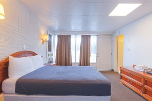 A hotel room with a large bed, a wooden dresser, a nightstand, and a window with curtains. - Sonrise Inn Lincoln Hwy By OYO (Breezewood)