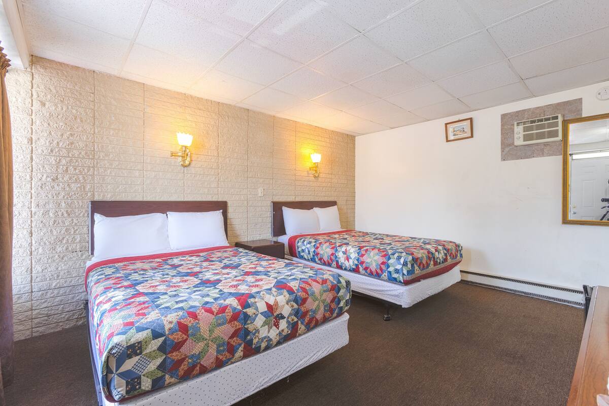 Camera d'albergo con due letti, ciascuno con copripiumino trapuntato, una parete in mattoni e due lampade a parete.