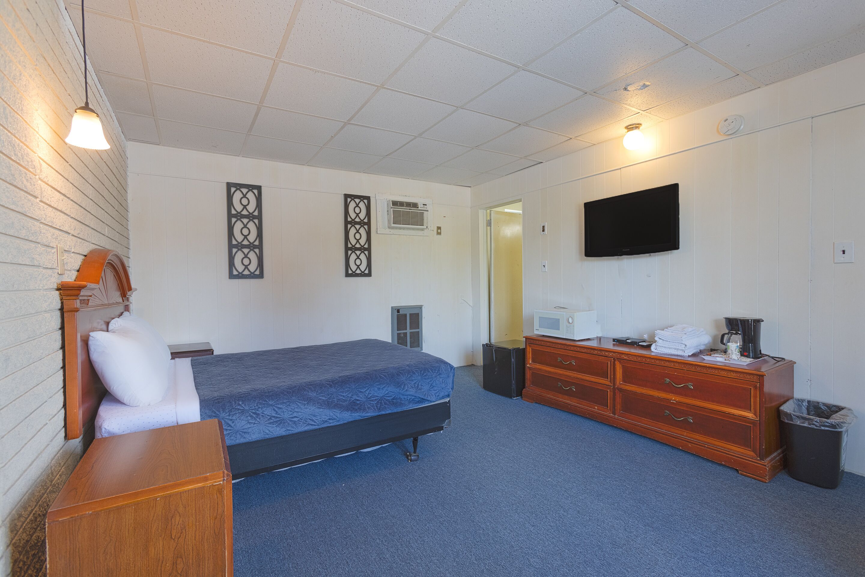 Une chambre d’hôtel avec un lit, une commode, une télévision et une poubelle.