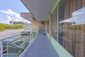 A covered walkway with a metal railing, a fire extinguisher, and a view of a road with cars. - Sonrise Inn Lincoln Hwy By OYO (Breezewood)