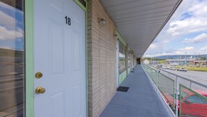 A hotel corridor with a white door marked "18", a brick wall, and a covered walkway with a metal railing overlooking a road with cars. - Sonrise Inn Lincoln Hwy By OYO (Breezewood)