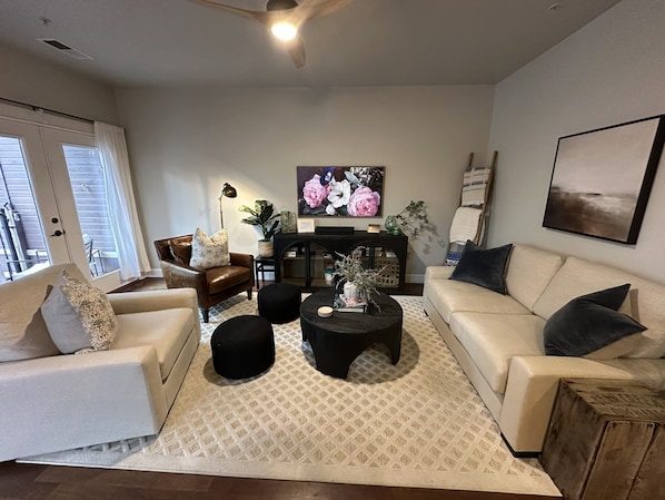 Un salon comprenant un canapé, des fauteuils, des poufs, une table basse, une cheminée et un ventilateur de plafond.