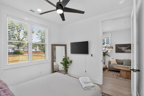Et soveværelse med seng, ventilator, fjernsyn og et vindue med persienner.