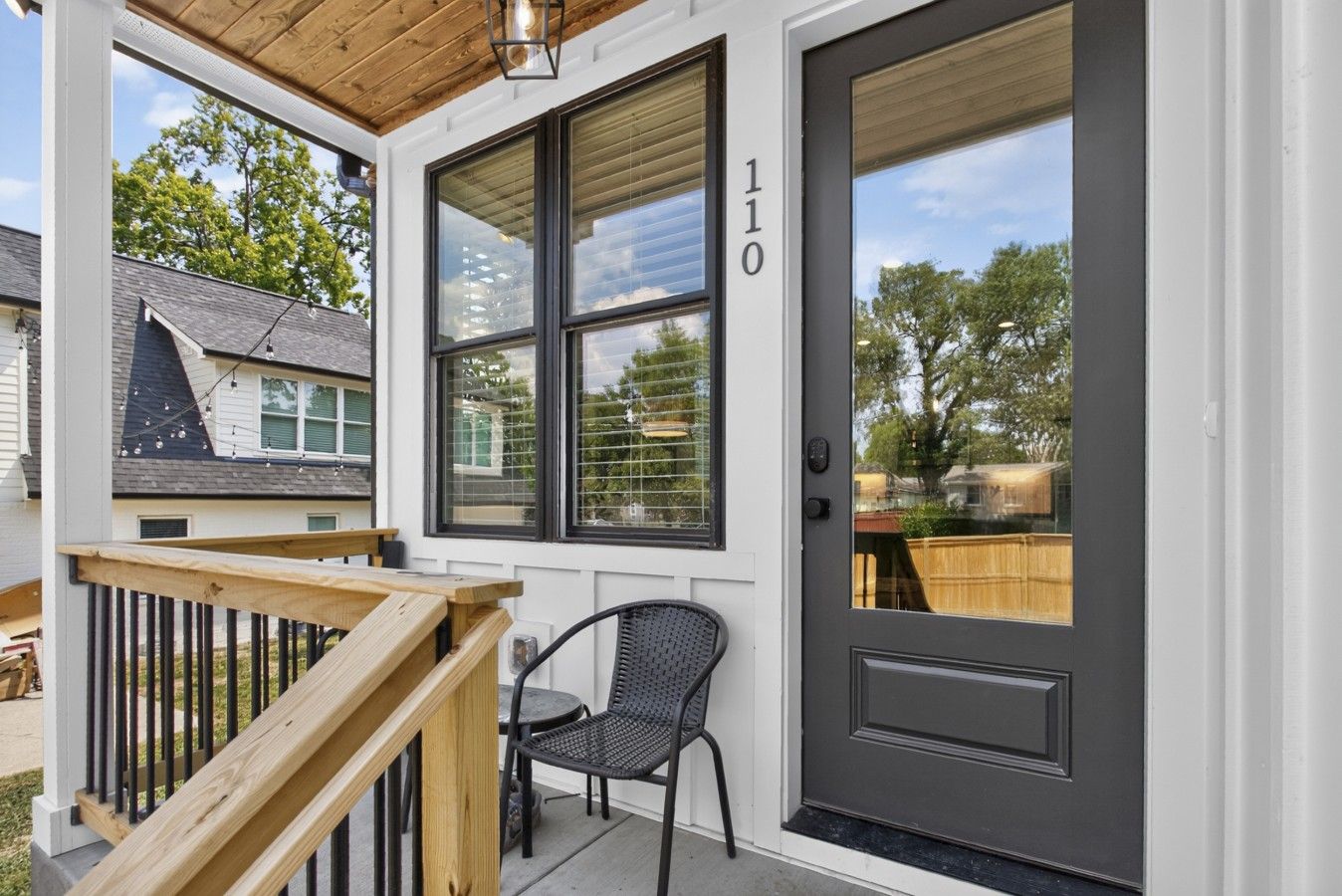 A residential entryway with a dark front door, a wooden staircase, and a small outdoor seating area.