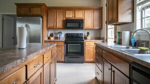 Une cuisine avec des meubles en bois, un réfrigérateur en acier inoxydable, un four à micro-ondes, un four traditionnel et un évier avec un robinet.