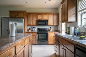 A kitchen with wooden cabinets, a stainless steel refrigerator, a microwave, an oven, and a sink with a faucet. - Sleeps 14 on a Duck River ranch: 4 en suite bedrooms, patio, fishing, horses (Normandy)