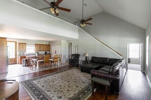 A spacious living room with a large dark leather sofa, a dining area with wooden chairs, and a kitchen with wooden cabinets. - Sleeps 14 on a Duck River ranch: 4 en suite bedrooms, patio, fishing, horses (Normandy)