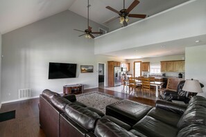 A spacious living area with a large leather sofa, a flat-screen TV, and a dining area with wooden furniture. - Sleeps 14 on a Duck River ranch: 4 en suite bedrooms, patio, fishing, horses (Normandy)