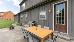 Un bâtiment en bois doté d’un patio comprenant une table et des chaises, un barbecue et un foyer.