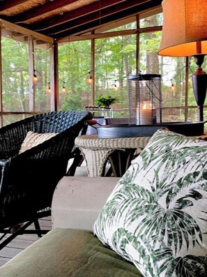Relax on the enclosed porch with a wicker chair and cushioned bench, surrounded by lush greenery.