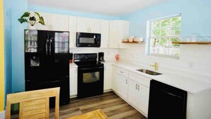 Una cocina compacta con armarios blancos, un refrigerador negro, un microondas, una estufa y un lavamanos.