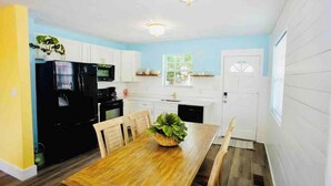 Cocina compacta con armarios blancos, un refrigerador negro, microondas y una mesa de comedor con sillas.