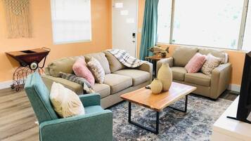 Un salon avec deux canapés, une table basse, un téléviseur et une grande fenêtre avec des rideaux.