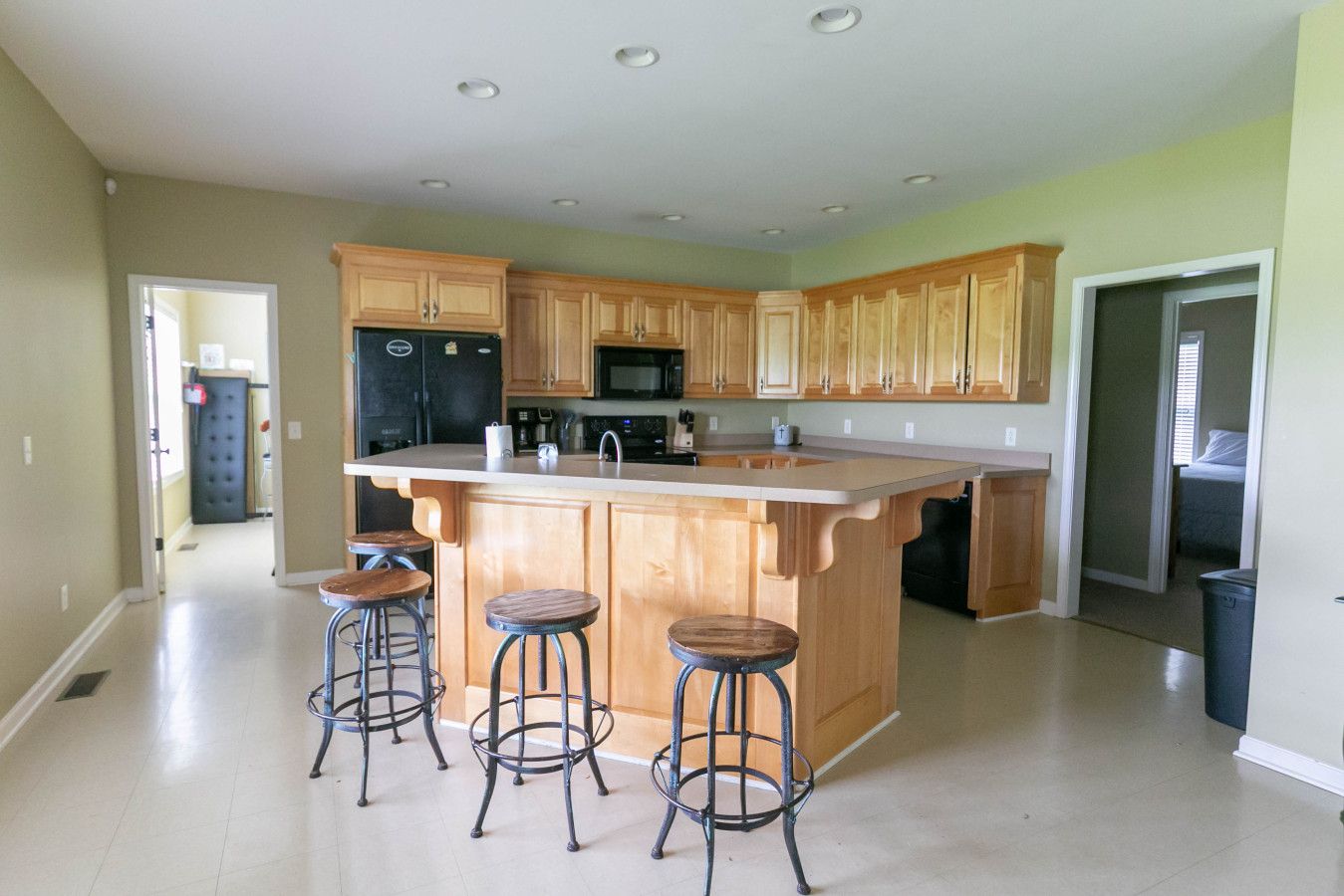 A spacious kitchen with wooden cabinets, a central island with stools, and a refrigerator.