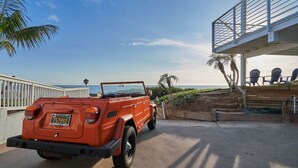 Un Jeep rojo estacionado en una entrada con vista al océano y una palmera.