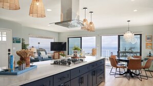 Una cocina moderna con una isla grande, armarios oscuros y un comedor con sillas color naranja.