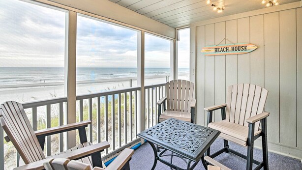Une terrasse couverte, dotée de chaises Adirondack et d’une table, qui offre une vue sur la plage.