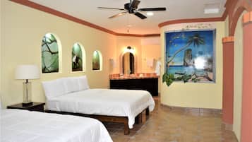 Habitación de hotel con dos camas, ventilador de techo, un cuadro de paisaje tropical y piso de baldosas.