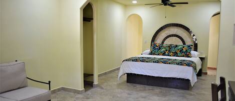 Un dormitorio con cama, una silla, ventilador de techo y un arco decorativo en la pared.