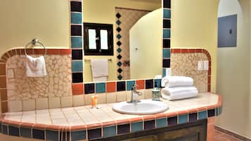 A bathroom with a tiled vanity, a sink, a mirror, and a towel rack.