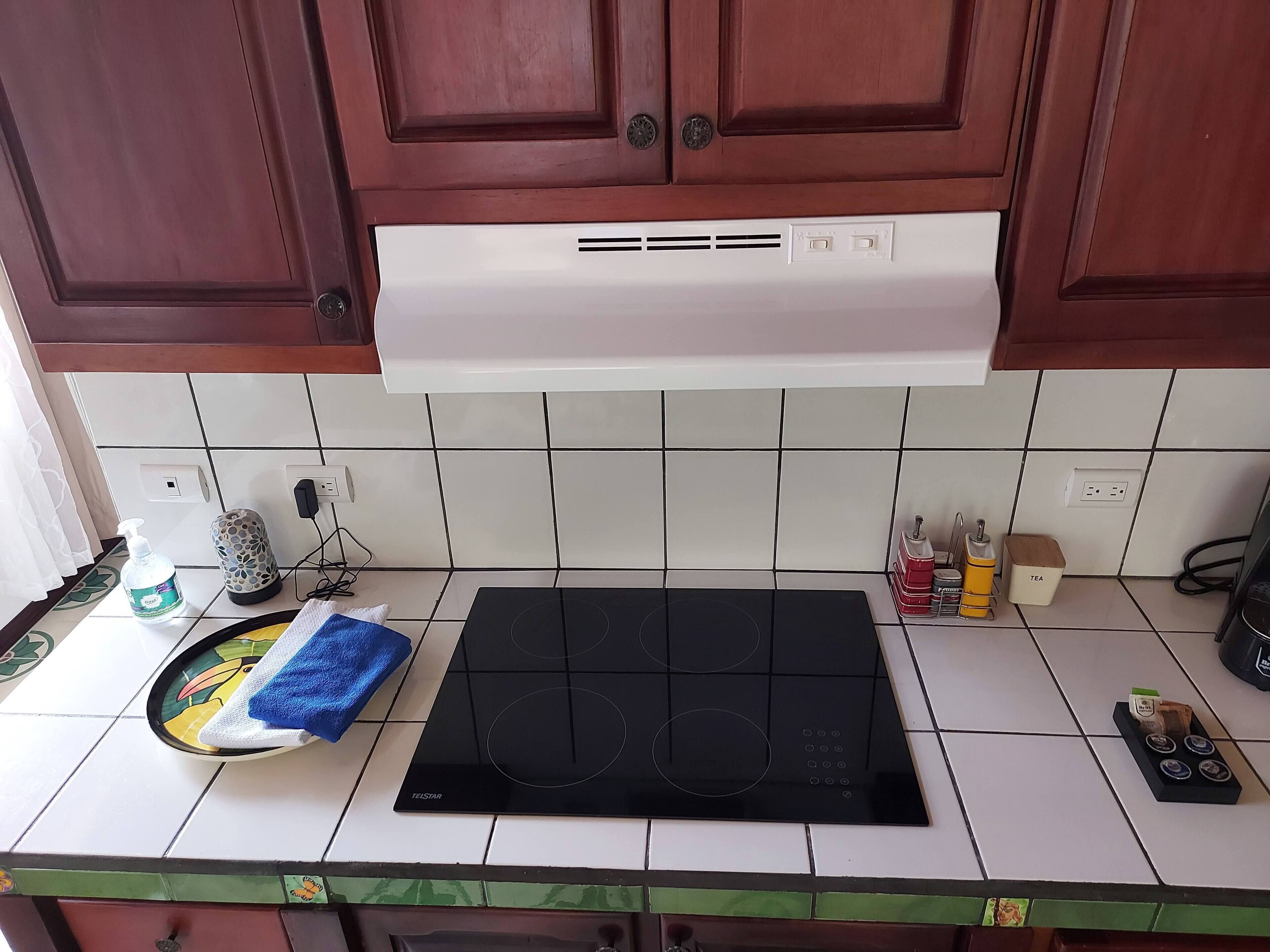 A kitchen with a black induction cooktop, white tiled backsplash, and wooden cabinets.