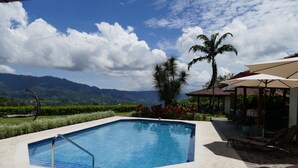 A swimming pool with a view of mountains, a palm tree, and outdoor seating. - BUNGALOWS SANLAZ (Jesús)