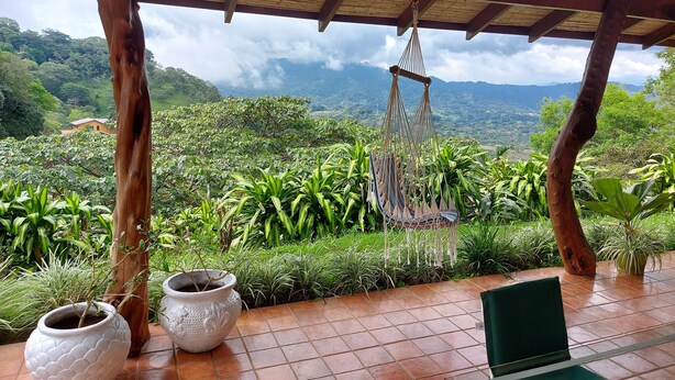 A covered outdoor area with a hammock, potted plants, and a view of a lush landscape. - BUNGALOWS SANLAZ (Jesús)