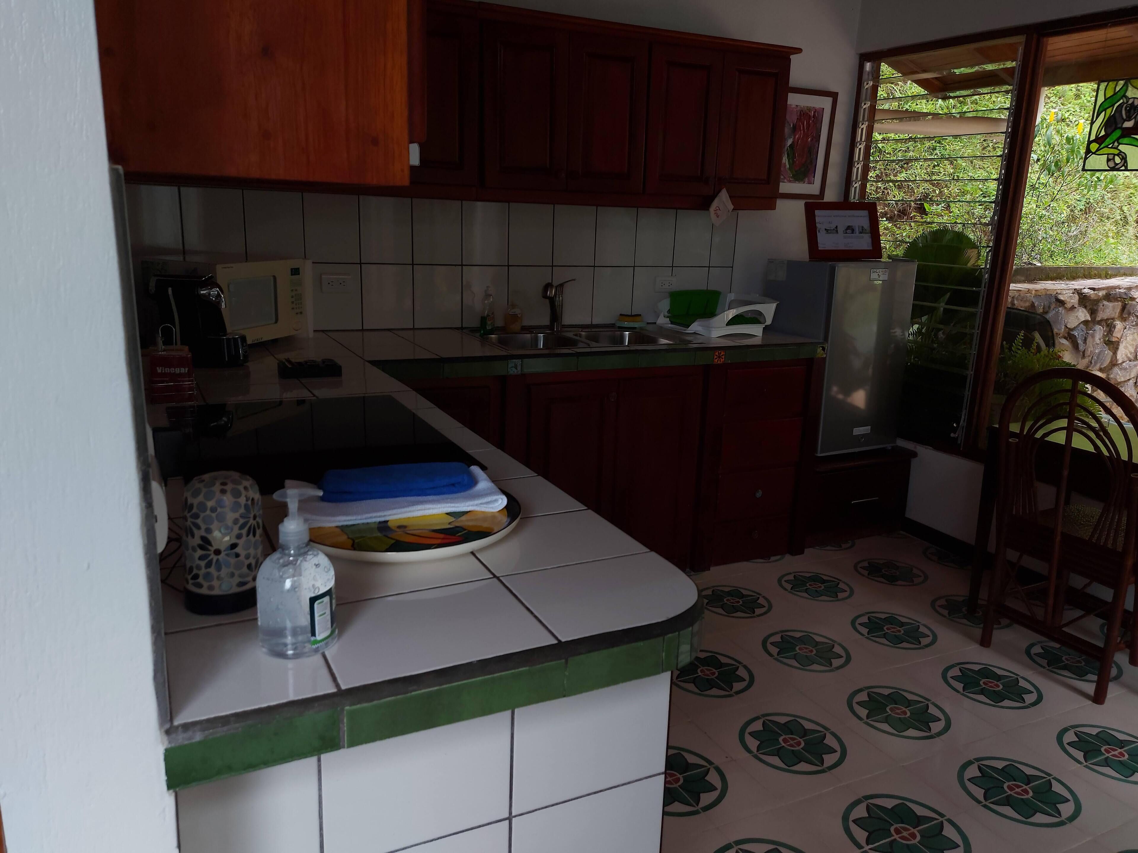 A kitchen with wooden cabinets, a tiled backsplash, and a countertop with a water bottle and a dish rack.