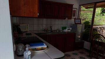 A kitchen with wooden cabinets, a tiled backsplash, and a countertop with a water bottle and a dish rack.