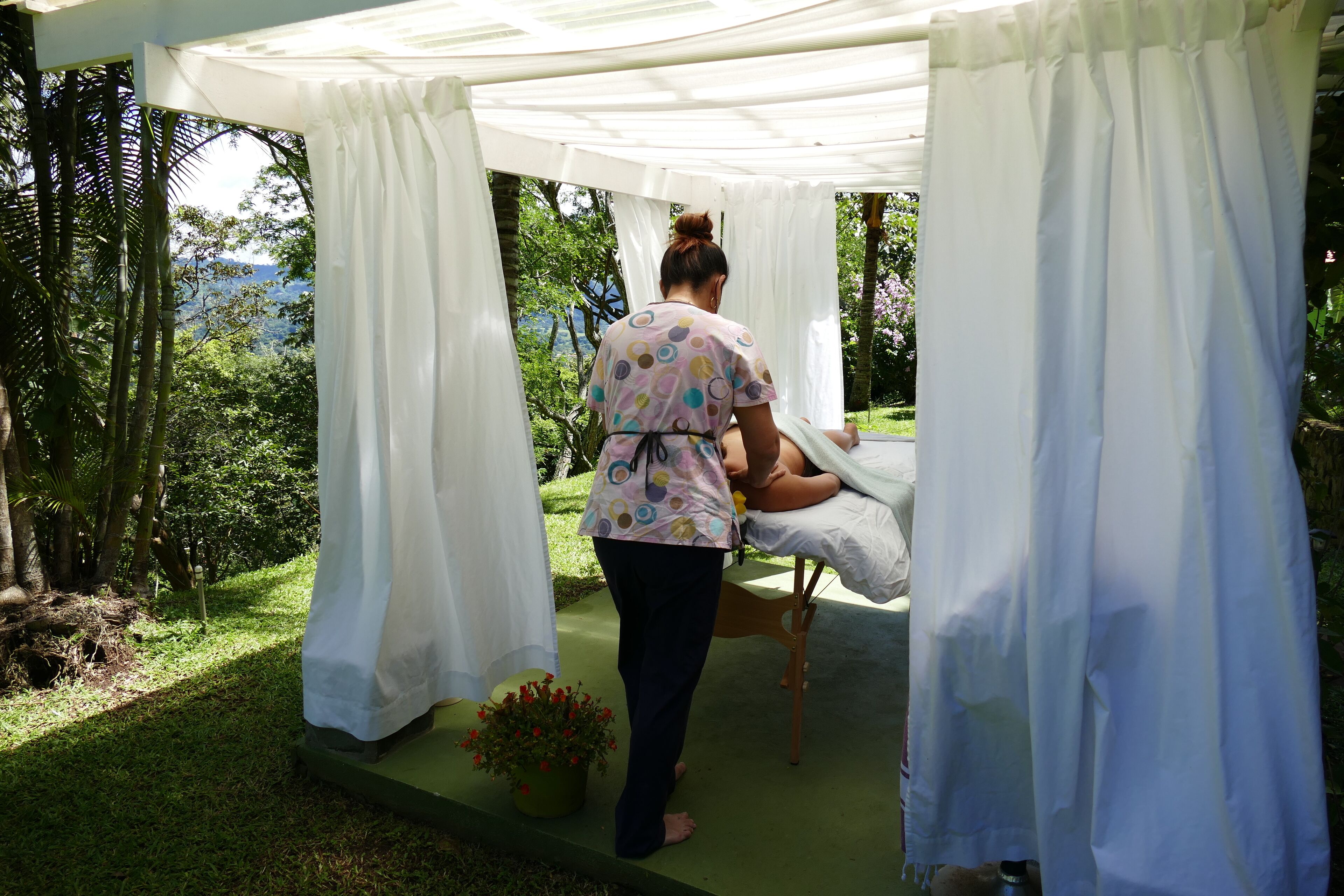 Une personne s’occupe d’un patient dans un espace extérieur abrité, avec vue sur la verdure et une montagne au loin.