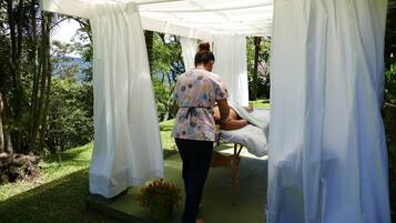 Une personne s’occupe d’un patient dans un espace extérieur abrité, avec vue sur la verdure et une montagne au loin.