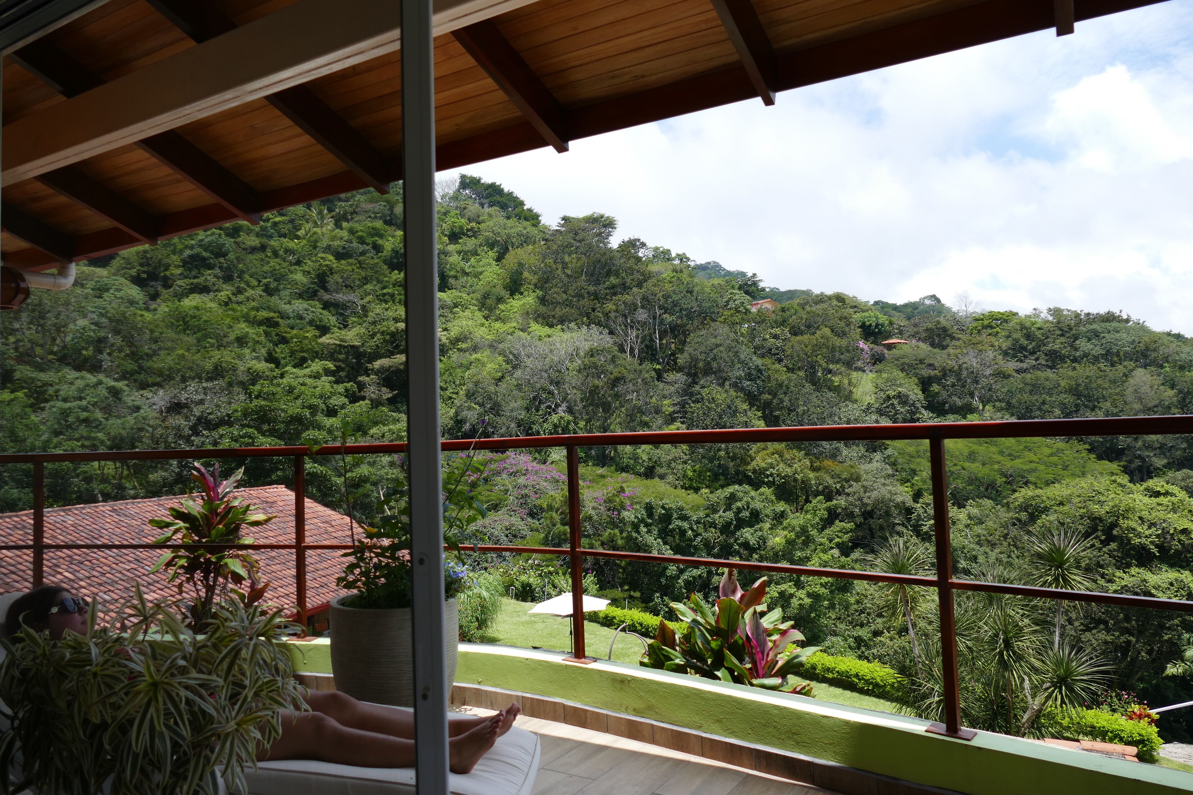 A balcony with a view of a lush green landscape and a red-roofed building in the distance.