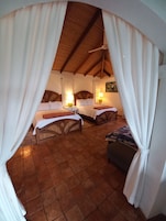 Um quarto aconchegante com duas camas, um banco e um ventilador de teto.
