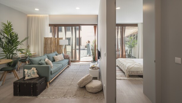 A modern living room with a sofa, a coffee table, and a suitcase. There is a large window with curtains, a plant, and a view of the outside. - In the city centre - Cine Park Residence I (Funchal)