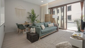 A modern living room with a green sofa, a dining table with chairs, a large window, and a potted plant. - In the city centre - Cine Park Residence I (Funchal)