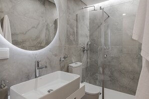 Un baño moderno con un lavamanos rectangular grande, una ducha con cerramiento de vidrio y un inodoro.