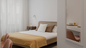 Ein Hotelzimmer mit Bett, Nachttisch mit Lampe, Sessel und einer Frühstückstafel mit einem Glas Saft.