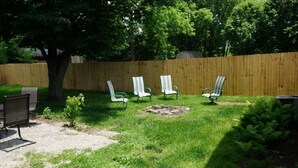 A backyard with a wooden fence, four lawn chairs, a small tree, and a grill.