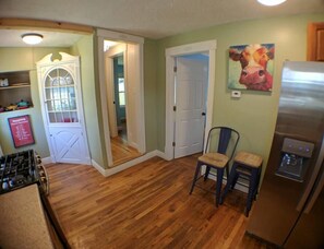 A kitchen with wooden flooring, a refrigerator, a chair, and a door leading to another room. - Harper, Two Bedroom House in Historic Loveland (Loveland)